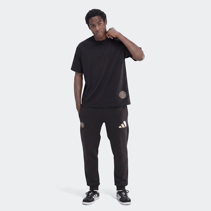 Black Sportswear Open Hem Single Jersey T-Shirt on a male model, paired with black Adidas sweatpants, standing in a studio.