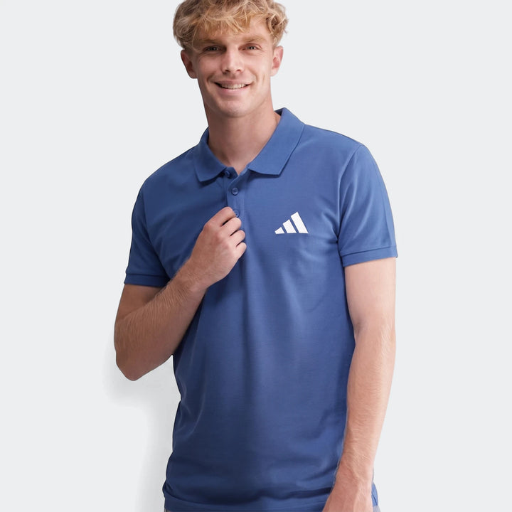 Smiling man wearing a blue Sportswear Slim Pique Polo Shirt with short sleeves, posing casually in a studio.