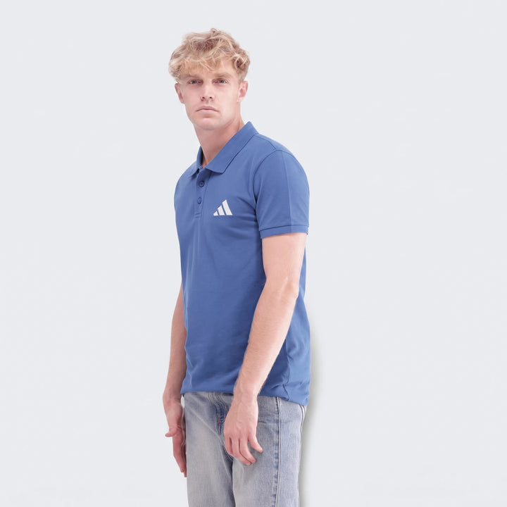 Male model wearing a blue Sportswear Slim Pique Polo Shirt and light wash jeans, captured from the waist up.