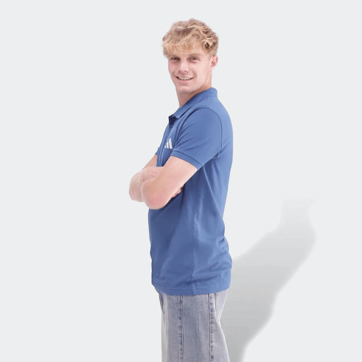 Young man wearing a blue Sportswear Slim Pique Polo Shirt and light blue jeans, with arms crossed and smiling.