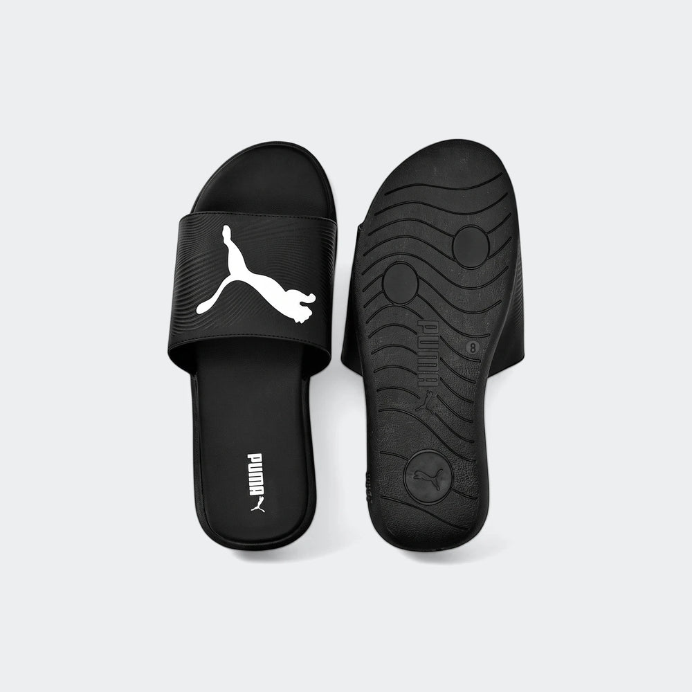 A pair of black Puma Sporty Embossed 2.0 slides, one facing up with the white logo and the other showing the textured sole.