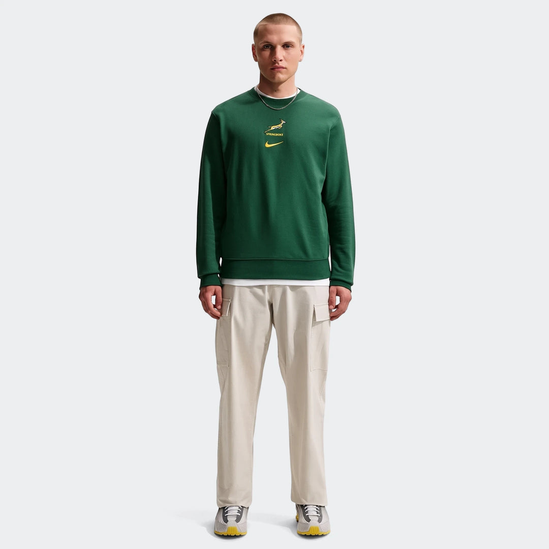 A male model wears a dark green Springboks Men's French Terry Crew sweatshirt with beige cargo pants and athletic shoes.