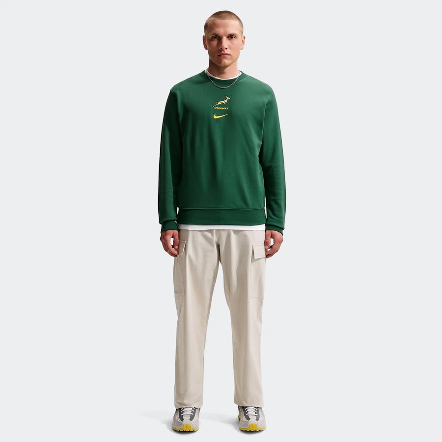 A male model wears a dark green Springboks Men's French Terry Crew sweatshirt with beige cargo pants and athletic shoes.