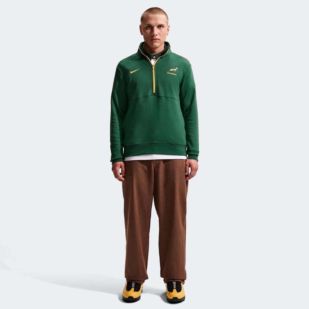Full body shot of a male model wearing a dark green Springboks Men's Nike 1/2 Zip Sweater with a yellow zipper, brown pants,
