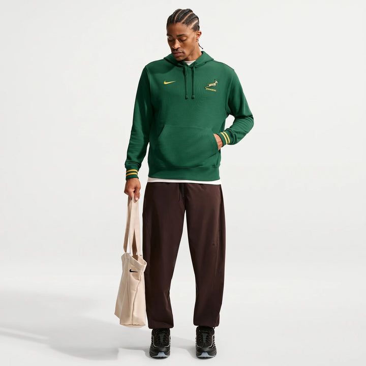 Male model showcases a green Nike Springboks men's hoodie, featuring yellow striped cuffs and branding, paired with brown