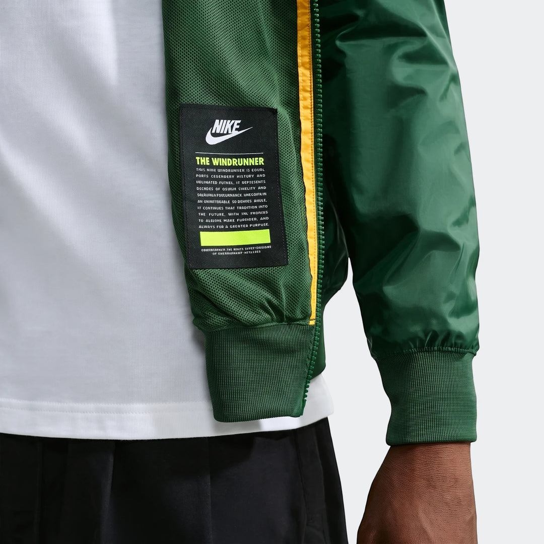 Close-up of a person wearing a dark green Springboks Nike Windrunner jacket with a yellow stripe and logo on a black label.