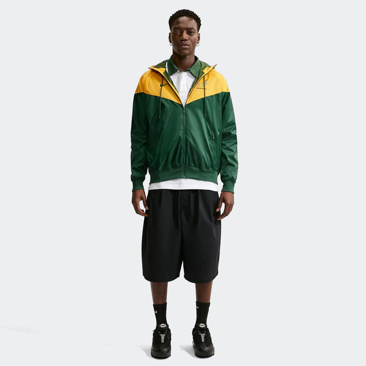 Full body shot of a male model wearing a green and yellow Springboks Nike Windrunner jacket with black shorts and sneakers.