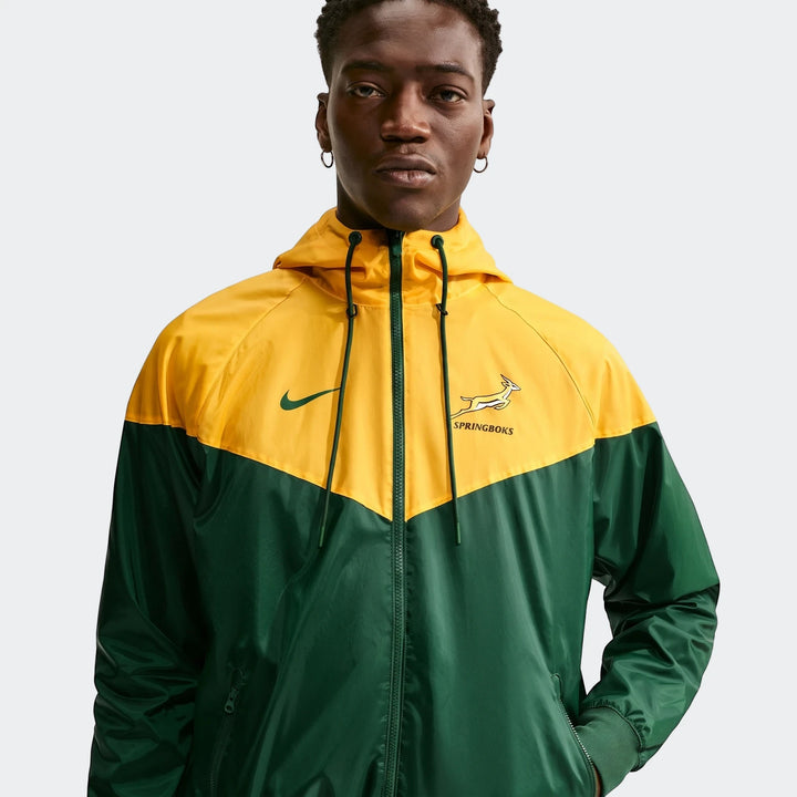 Close-up of a male model wearing a Springboks Nike Windrunner jacket in green and yellow, featuring a hood and prominent