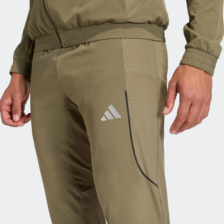 Technical Apparel Slim Pants in olive green, featuring an Adidas logo and patterned details, worn by a person for an