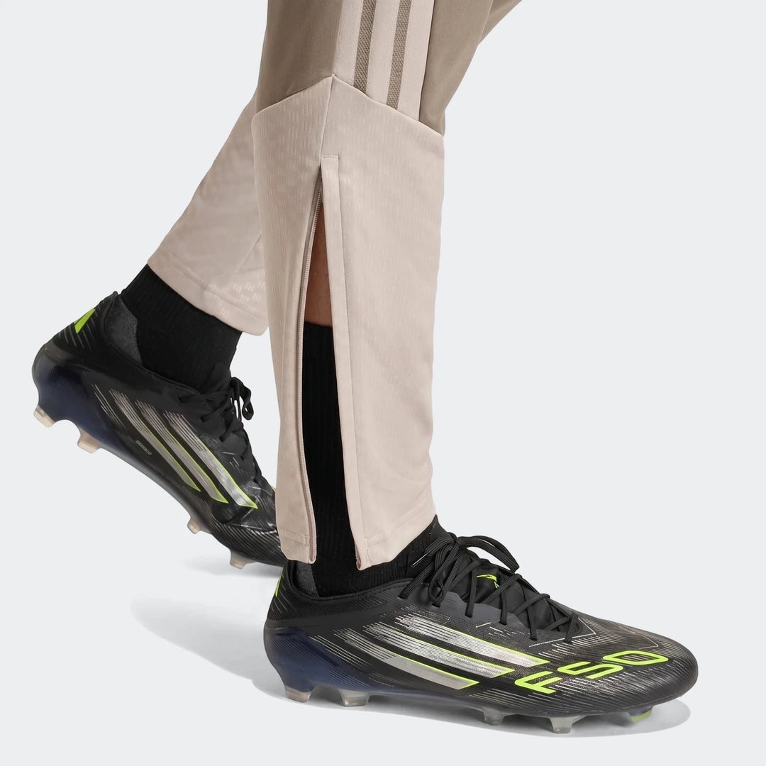 Close-up of a person's legs wearing Tior26C Pant brown athletic pants with side stripes and black football cleats.