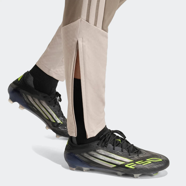 Close-up of a person's legs wearing Tior26C Pant brown athletic pants with side stripes and black football cleats.