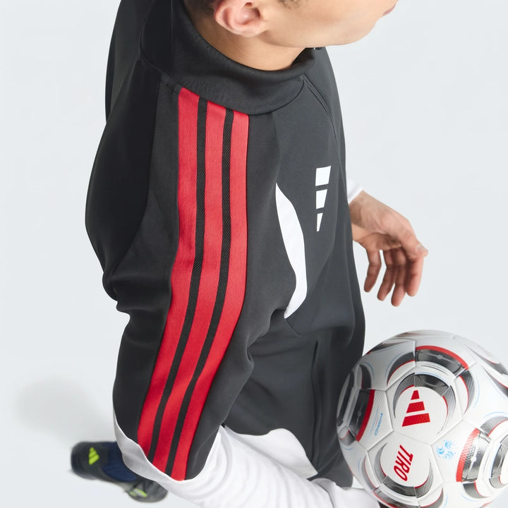 Close-up of a person wearing a black Tiro 26 Competition Training Jacket featuring distinctive red sleeve stripes, posing