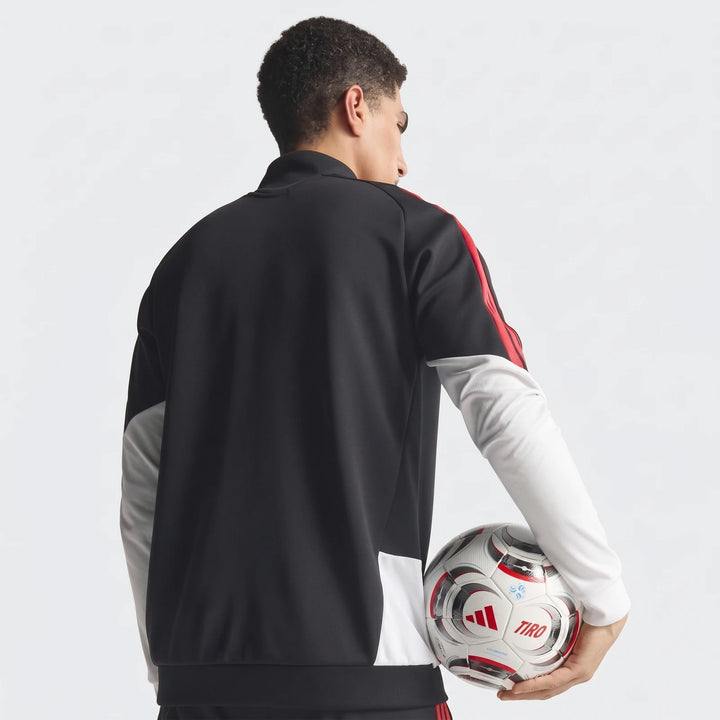 Man viewed from behind wearing a black Tiro 26 Competition Training Jacket with red stripes, holding a white soccer ball.