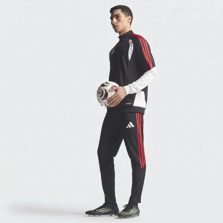 Male model wearing a black and red Adidas Tiro 26 Competition Training Jacket and matching pants, holding a soccer ball.