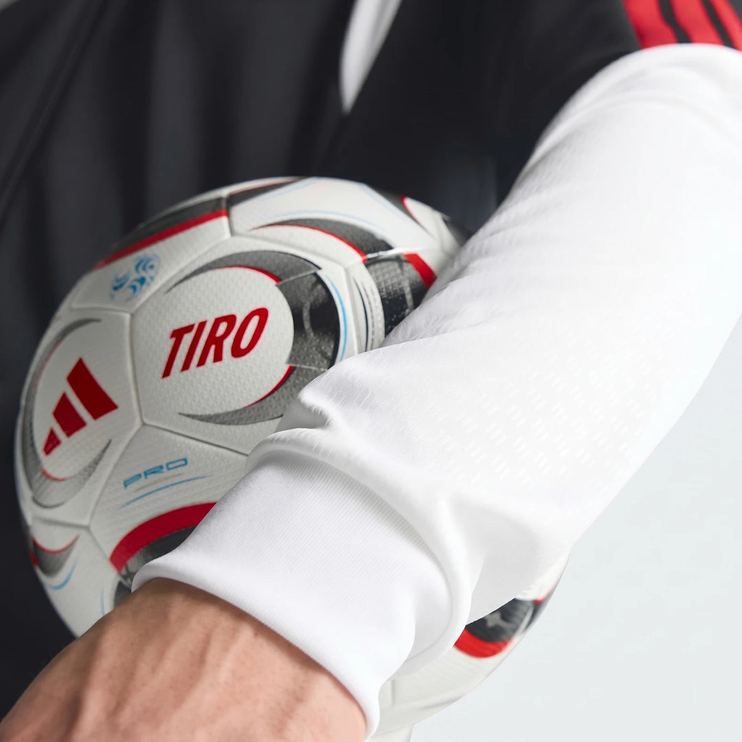 Close-up of a person wearing a black, white, and red Adidas Tiro 26 Competition Training Jacket, holding a white Tiro Pro