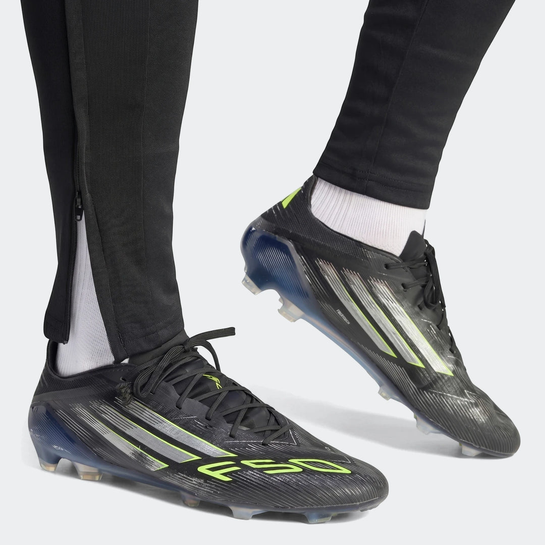 Close-up of a person wearing black Tiro 26 League Training Tracksuit Bottoms with zippers and black and neon green Adidas