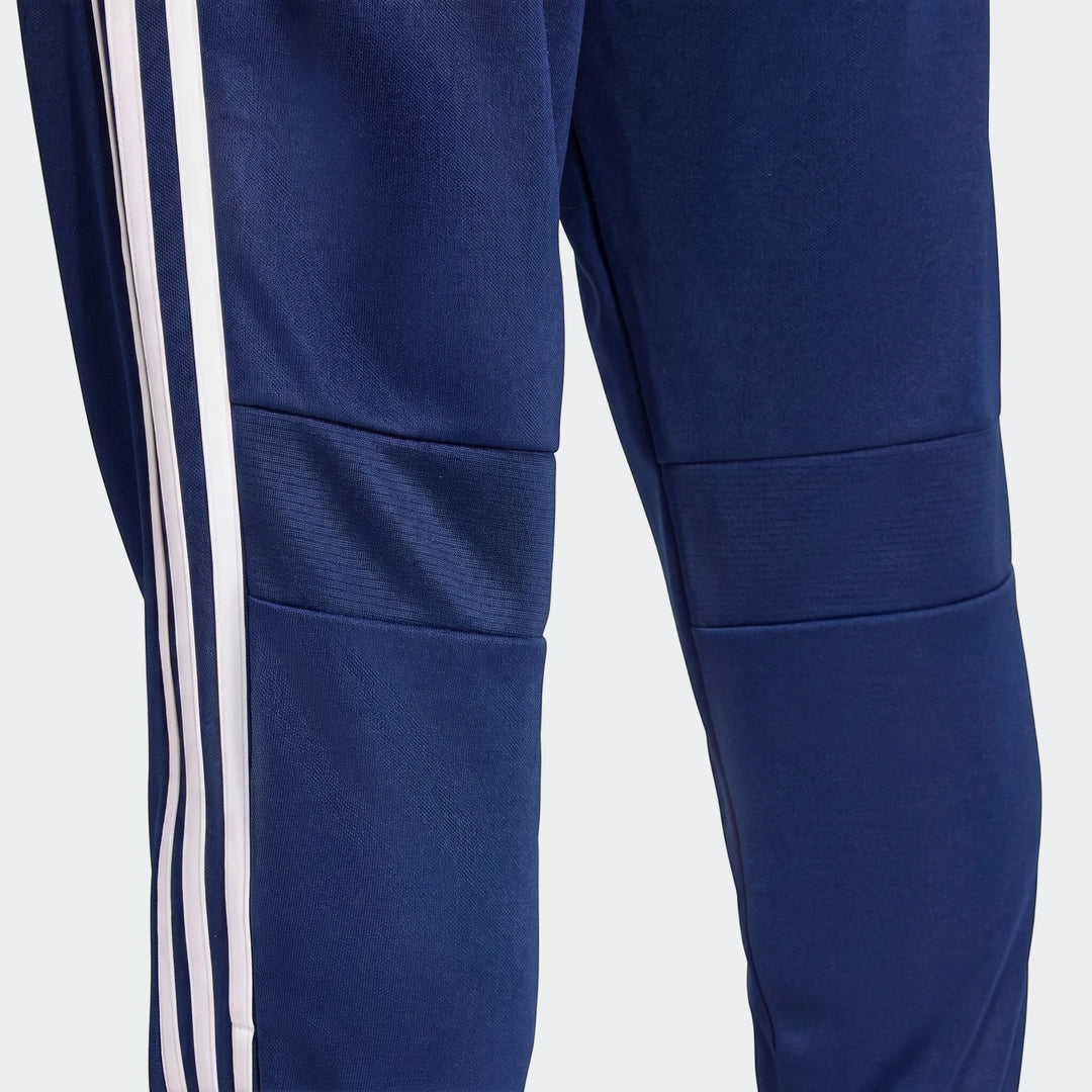 Close-up of men's navy blue Tiro Essentials Pants showing the athletic fit, knee panels, and white three-stripe detail on