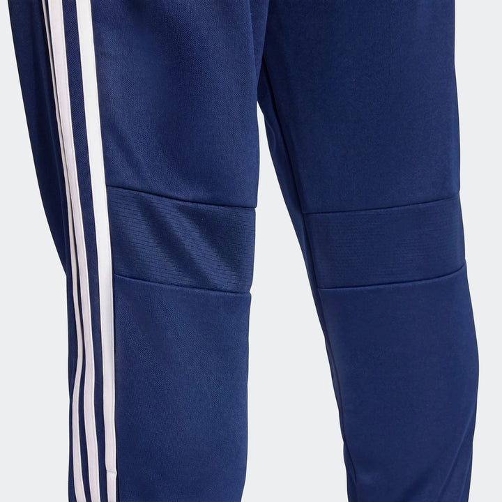 Close-up of men's navy blue Tiro Essentials Pants showing the athletic fit, knee panels, and white three-stripe detail on