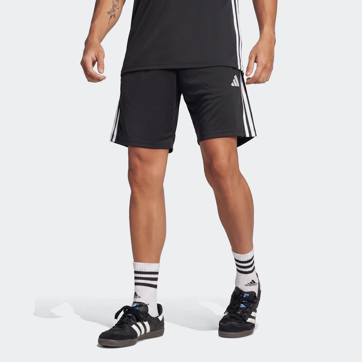 Male model wearing black Adidas Tiro Essentials Shorts with white stripes, black t-shirt, white socks, and black shoes.