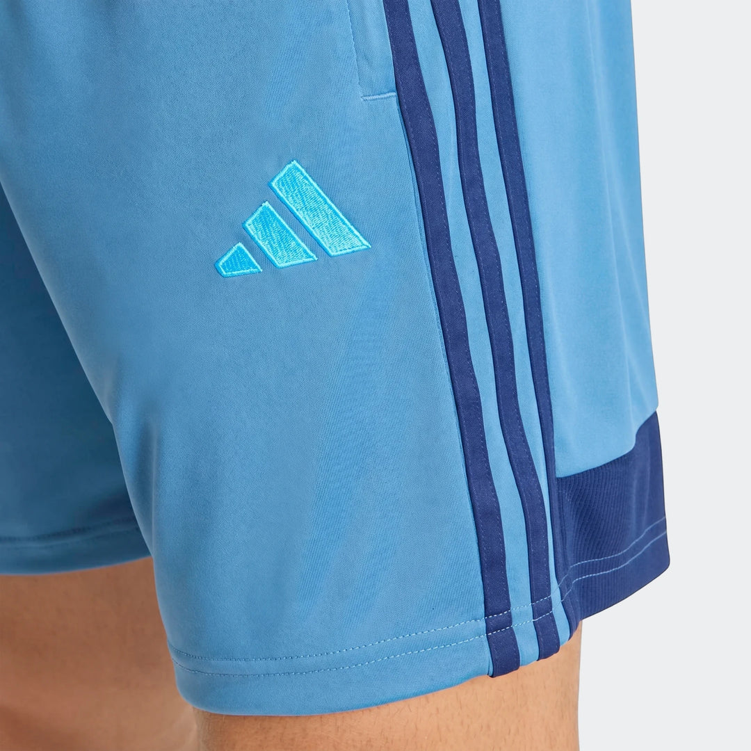 Light blue Adidas Tiro Essentials Shorts, with iconic three stripes and logo, worn on a model's leg in a close-up view.