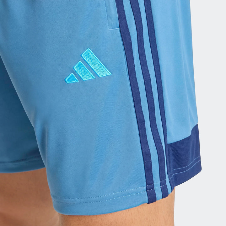 Light blue Adidas Tiro Essentials Shorts, with iconic three stripes and logo, worn on a model's leg in a close-up view.