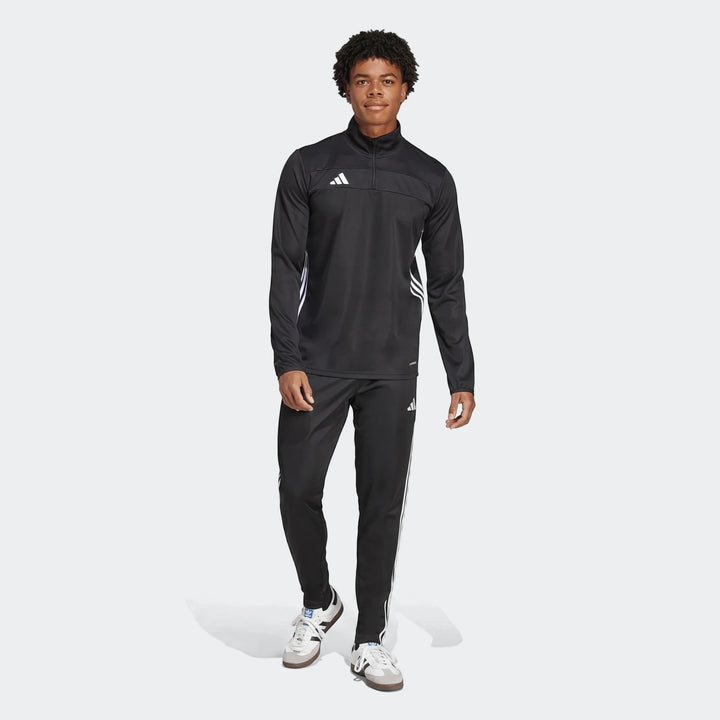 Full-body image of a male model wearing a black Adidas Tiro Essentials tracksuit, featuring a track top and matching pants,