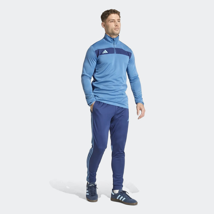 Male model wearing a blue Adidas Tiro Essentials Track Top and matching track pants, paired with blue sneakers, full body
