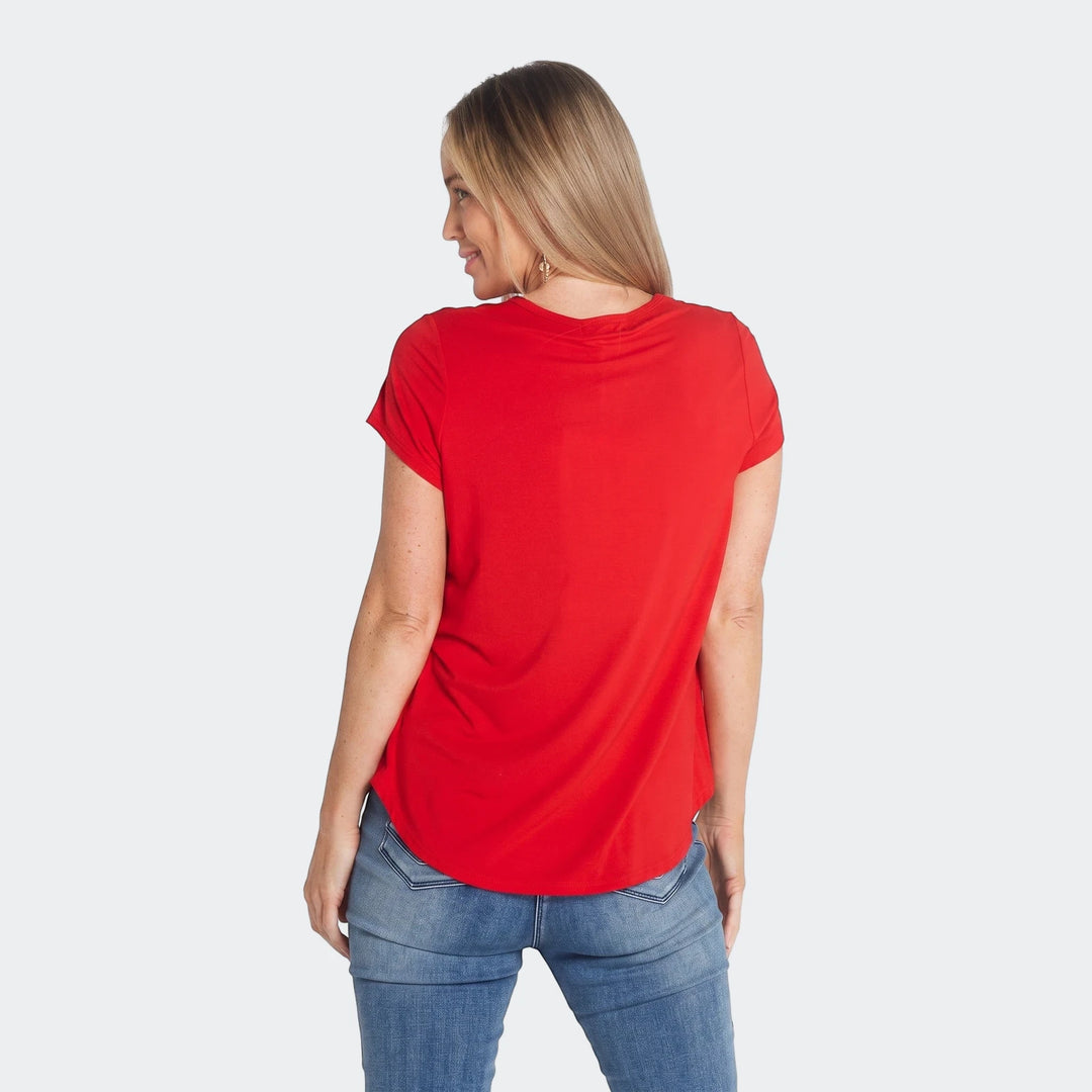 Rear view of a blonde woman wearing a red Tullio short-sleeve t-shirt and blue jeans, looking over her shoulder.