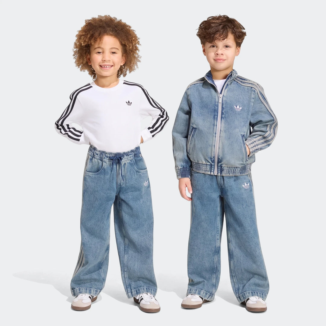 Two young children, a boy and a girl, smiling and posing in Adidas Firebird Loose Denim Track Pants and matching tops.