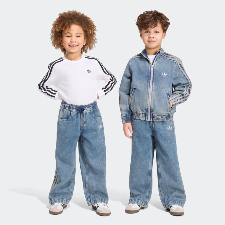 Two young children, a boy and a girl, smiling and posing in Adidas Firebird Loose Denim Track Pants and matching tops.