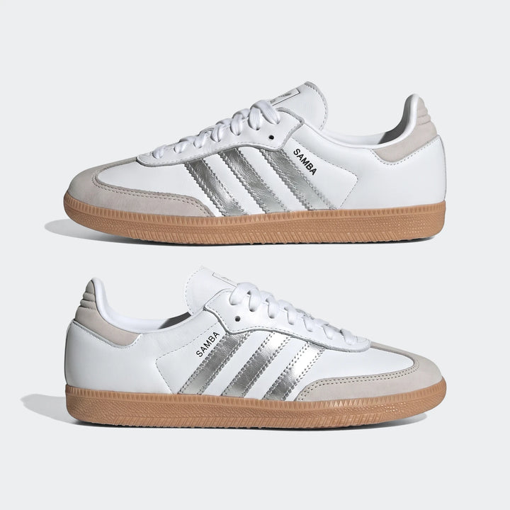 Two white Adidas Samba OG shoes with silver metallic stripes and gum rubber soles, displayed side-by-side.
