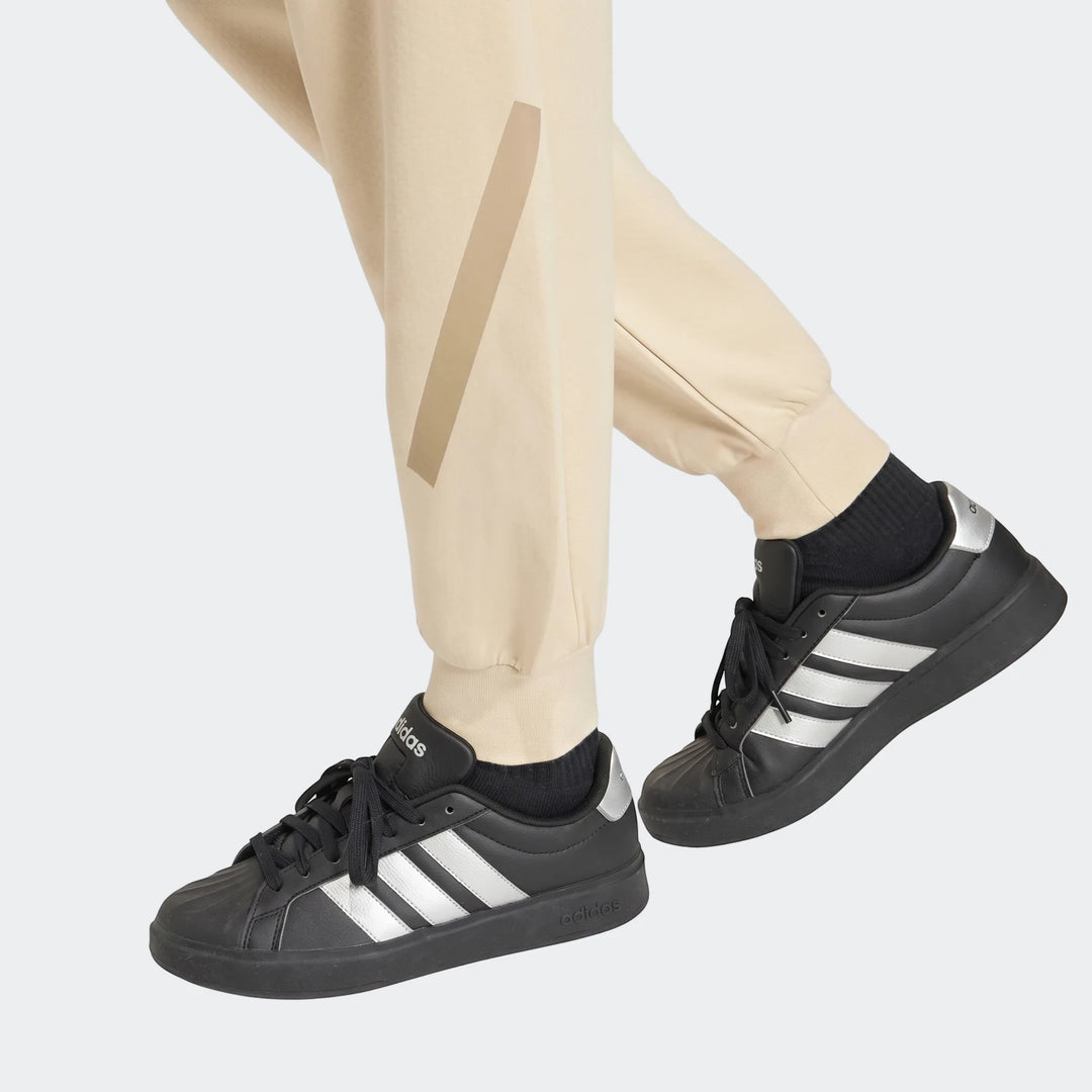 Close-up of a person wearing beige Adidas Z.N.E track pants with cuffs, paired with black Adidas sneakers featuring silver