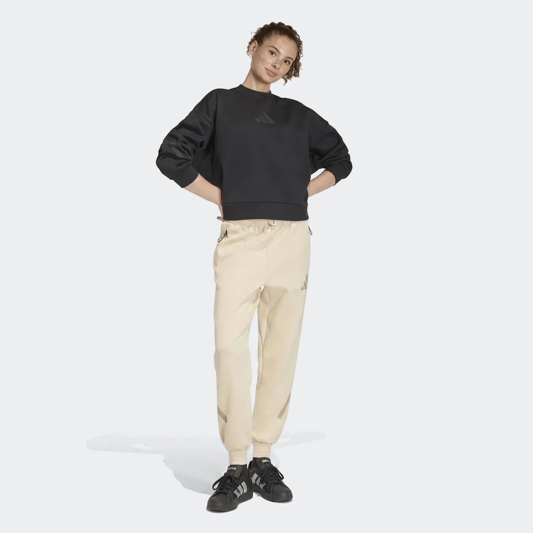 Female model in full body shot wearing a black sweatshirt and W Z.N.E Pt beige track pants with black sneakers.