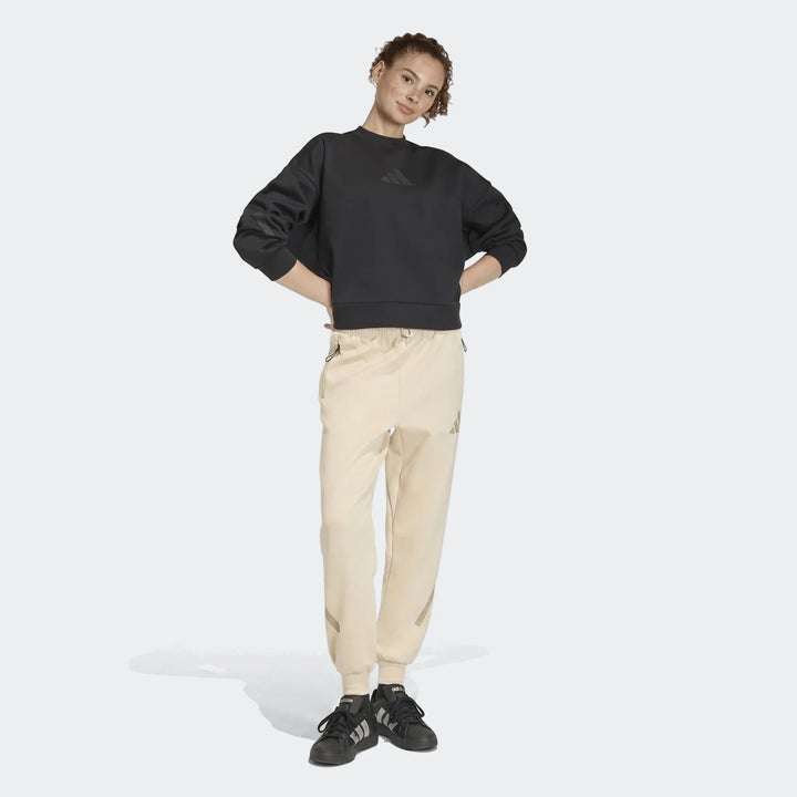 Female model in full body shot wearing a black sweatshirt and W Z.N.E Pt beige track pants with black sneakers.