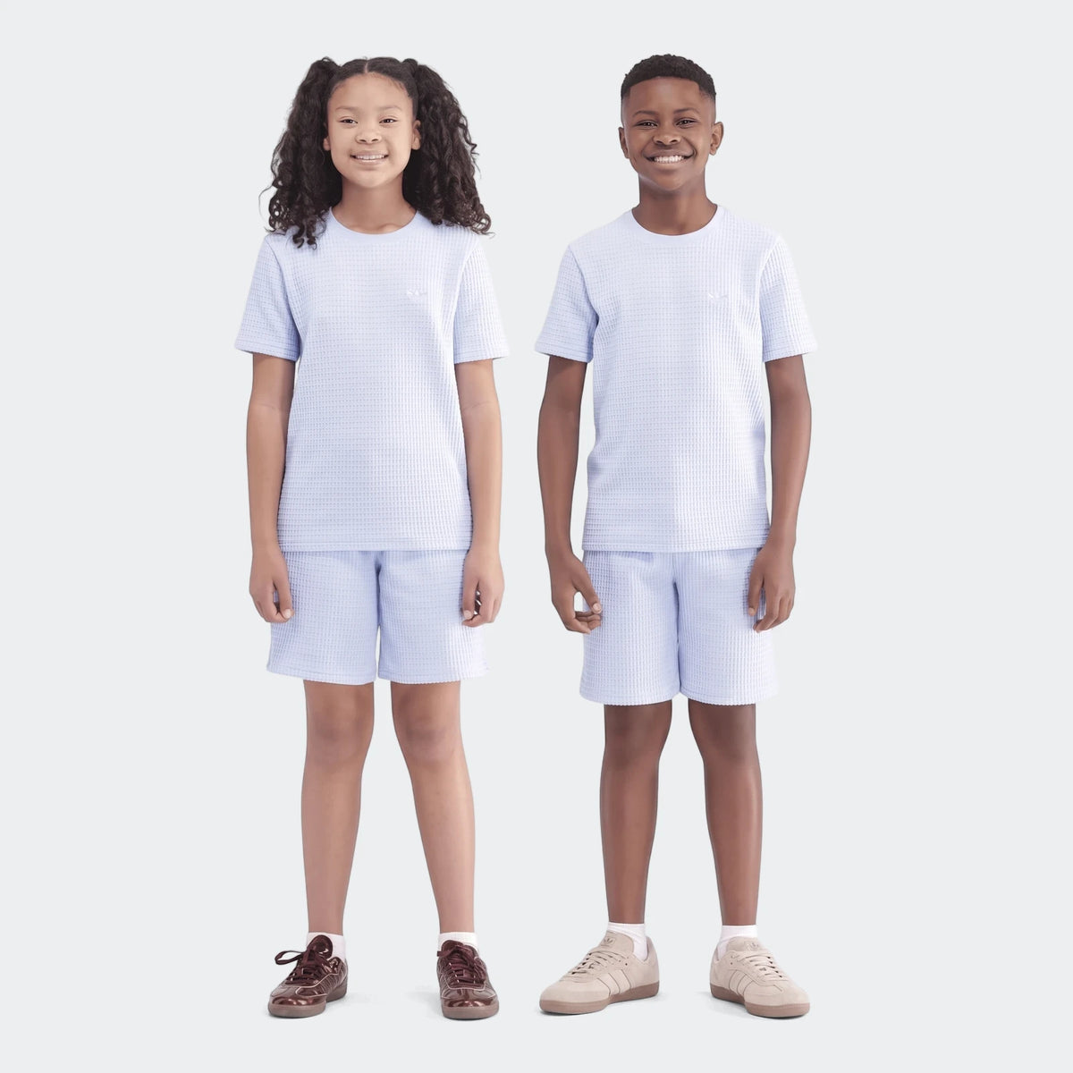 Two children, a boy and a girl, smiling while wearing light blue waffle knit t-shirt and shorts sets.