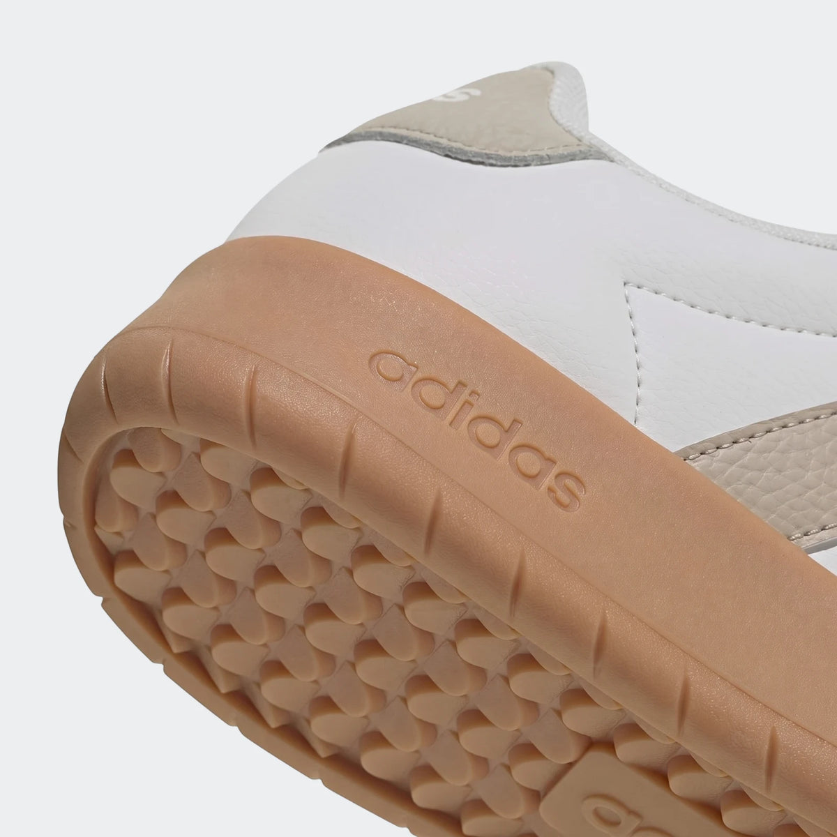 Close-up of white Adidas Barreda shoes featuring a tan gum sole with embossed 'adidas' branding and a textured tread pattern.
