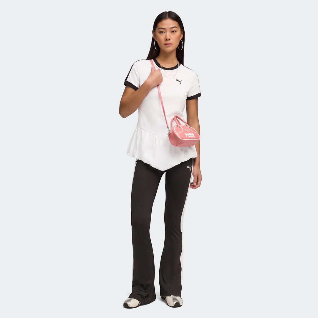 Model wears a white PUMA T7 Balloon Crew Neck Short Sleeve T-Shirt with a peplum hem, black track pants, and a pink mini bag.
