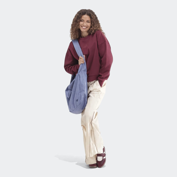 Woman smiles wearing a burgundy Slim Fleece Crew Sweatshirt, beige wide-leg pants, and carrying a blue shoulder bag.