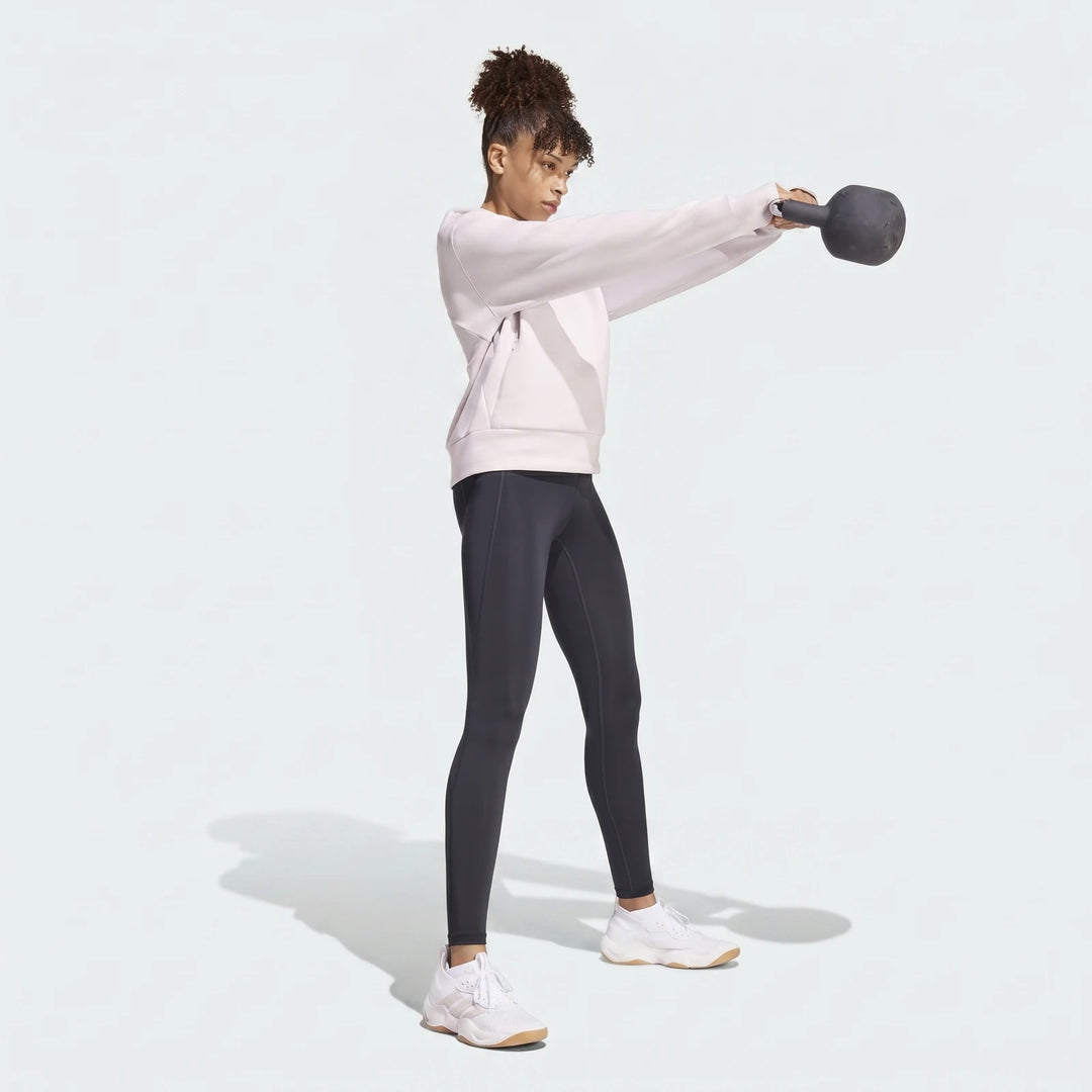 Woman in a light pink D4T Knit Crew Sweatshirt and dark gray leggings exercising with a kettlebell.