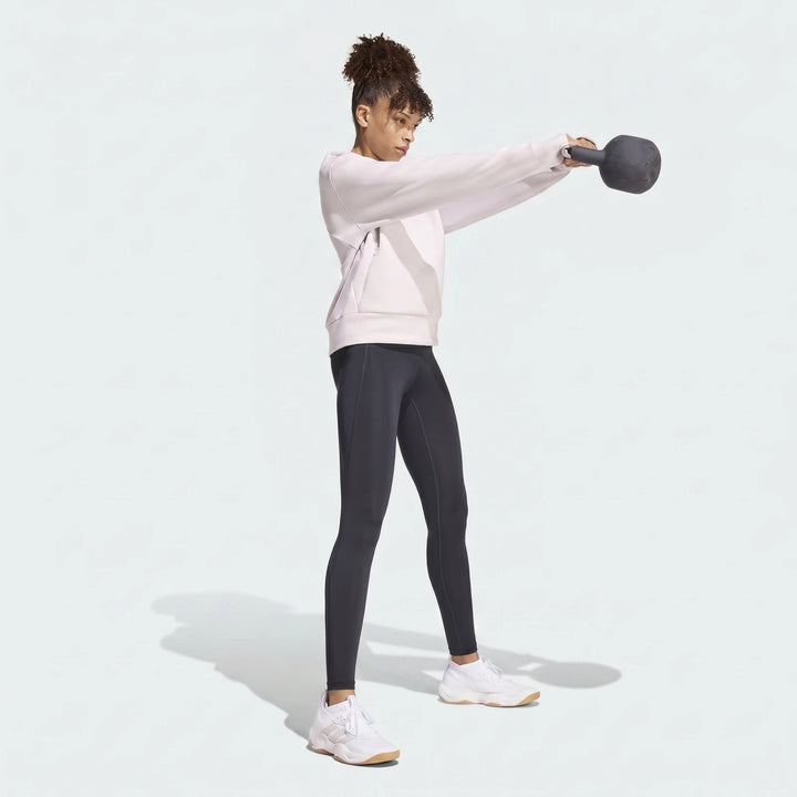 Woman in a light pink D4T Knit Crew Sweatshirt and dark gray leggings exercising with a kettlebell.