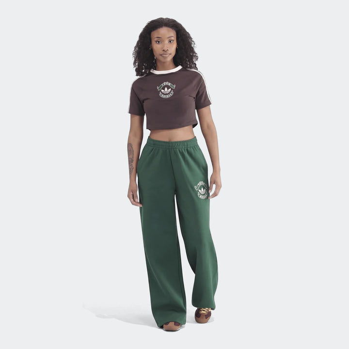 Full-body shot of a woman wearing green Infill Heritage Pants and a brown cropped t-shirt, showcasing the relaxed wide-leg