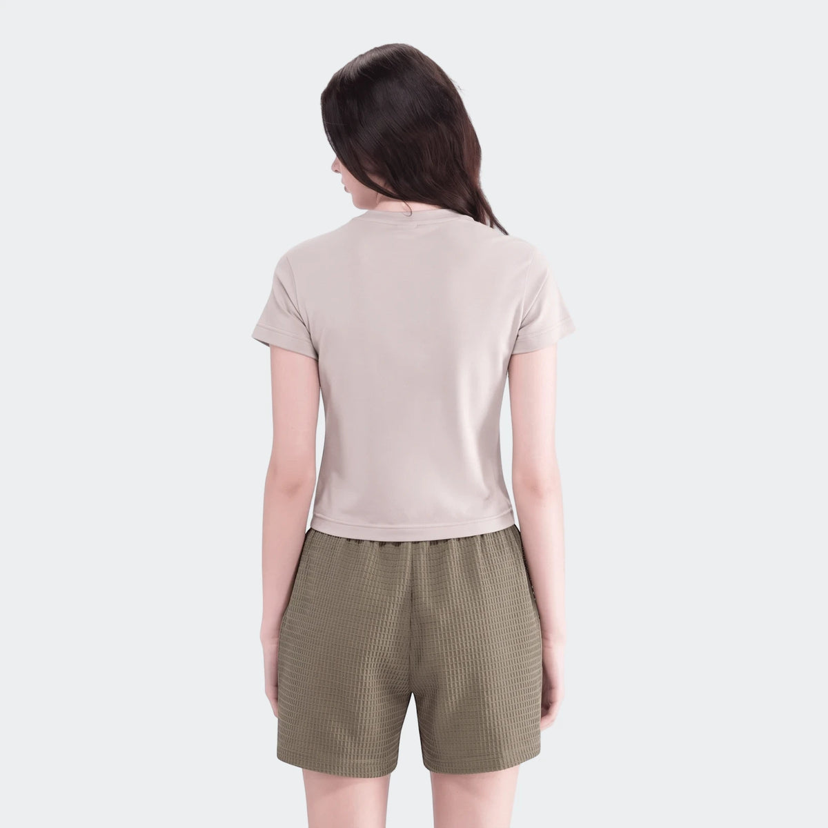Back view of a woman wearing a light beige short-sleeved t-shirt and olive green waffle knit Essential Shorts.