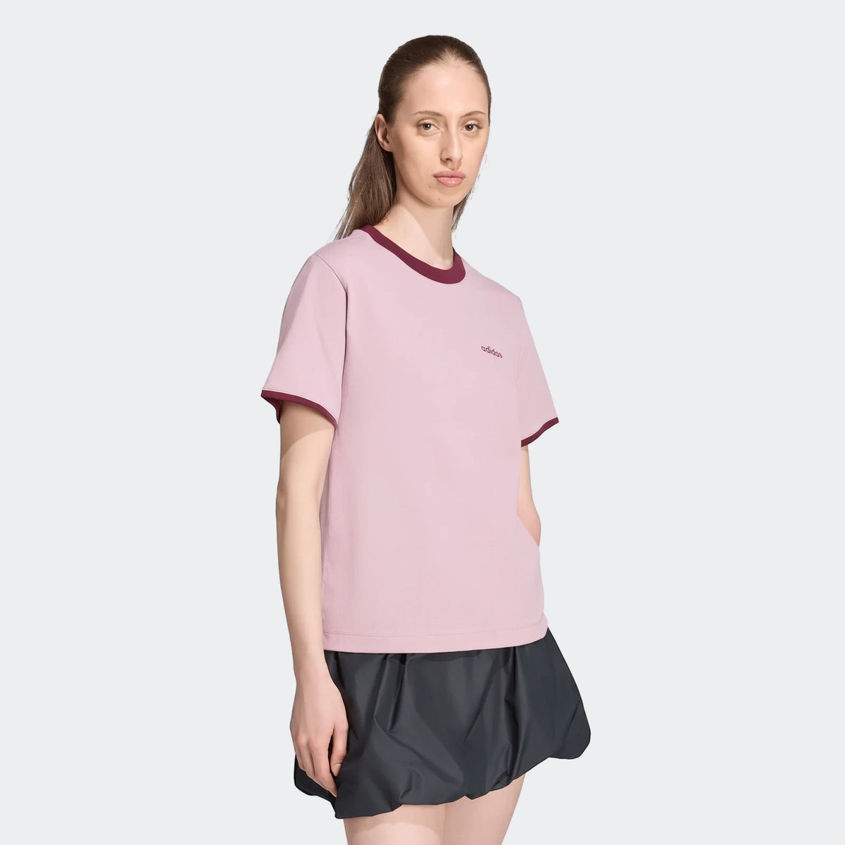Woman wearing a pink adidas Seasonal Essentials Colorpop T-Shirt with embroidered graphic and a dark grey skirt.
