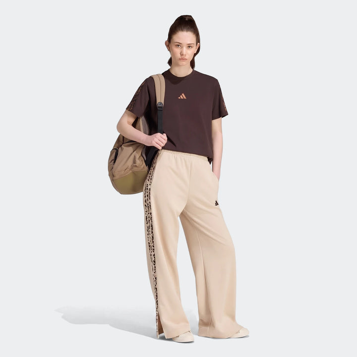 A woman wears a brown adidas t-shirt and Seasonal Essentials Animal Print 3-Stripes Joggers in beige, paired with a beige