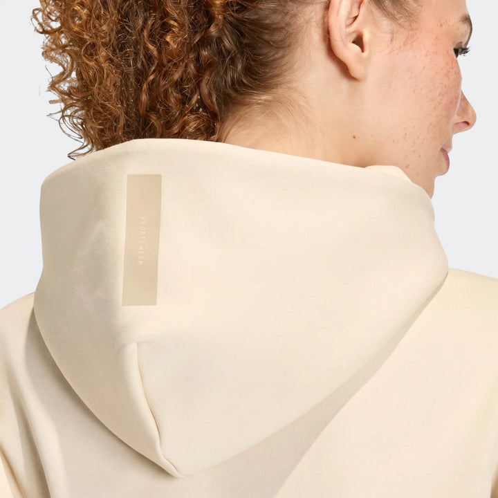 Back view of a woman wearing a beige W Z.N.E Fz hooded jacket, showcasing the hood and curly hair from behind.