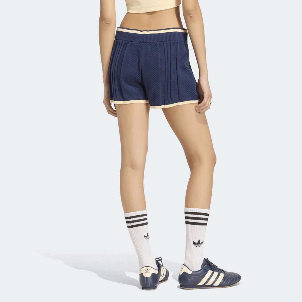 Model from behind wearing blue cable knit shorts with cream trim, white striped socks, and navy Adidas shoes. Rear view of