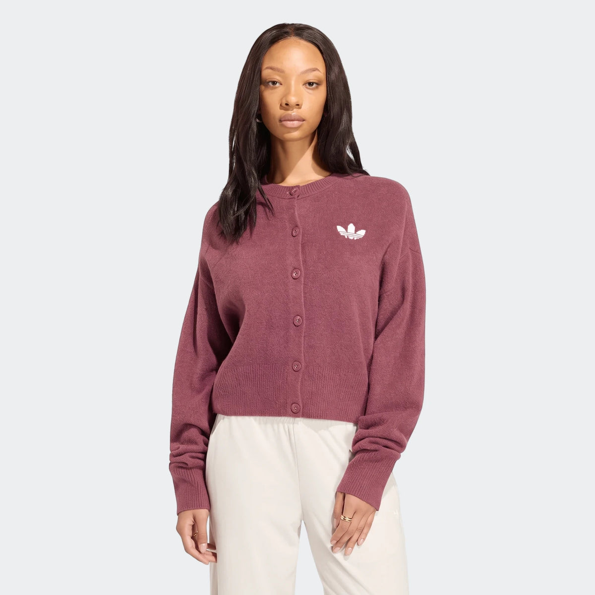 A female model wears a maroon Adidas Essentials Knit Cardigan with an embroidered white logo, styled with light pants.