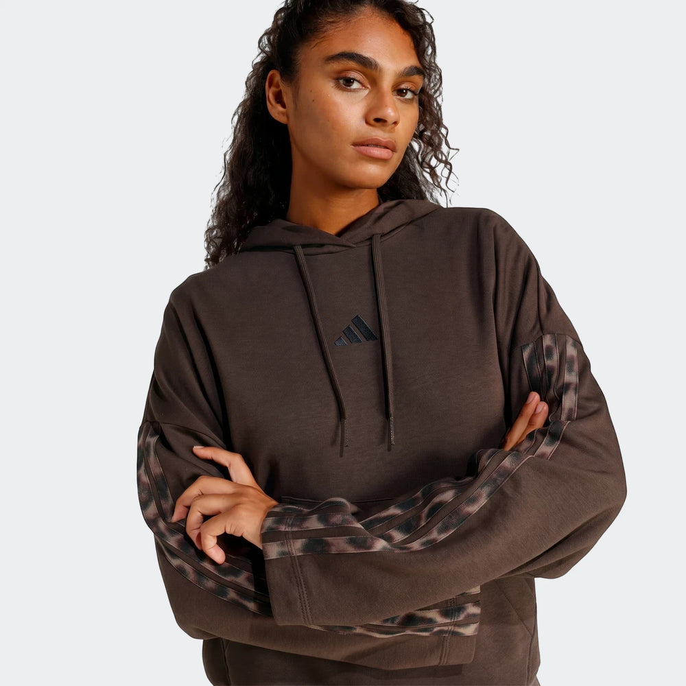 Waist-up view of a woman wearing a brown Adidas All-Over Print Infill French Terry Hoodie with leopard print stripes.