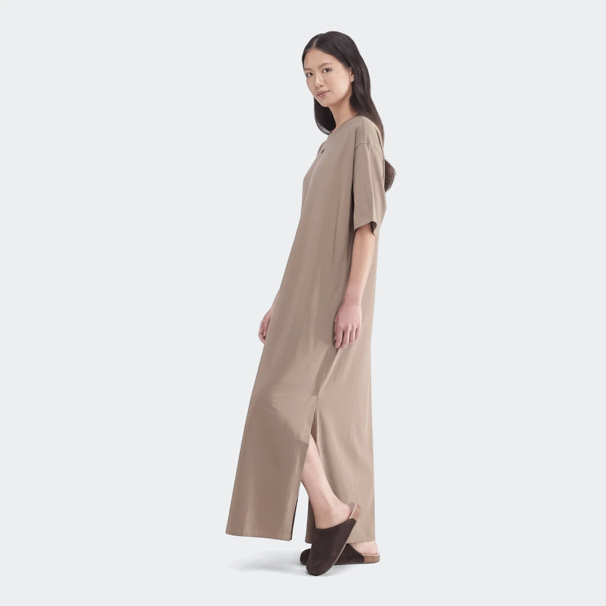 Full-length view of a woman wearing a loose-fitting, short-sleeved Essential Beige Dress with a side slit.