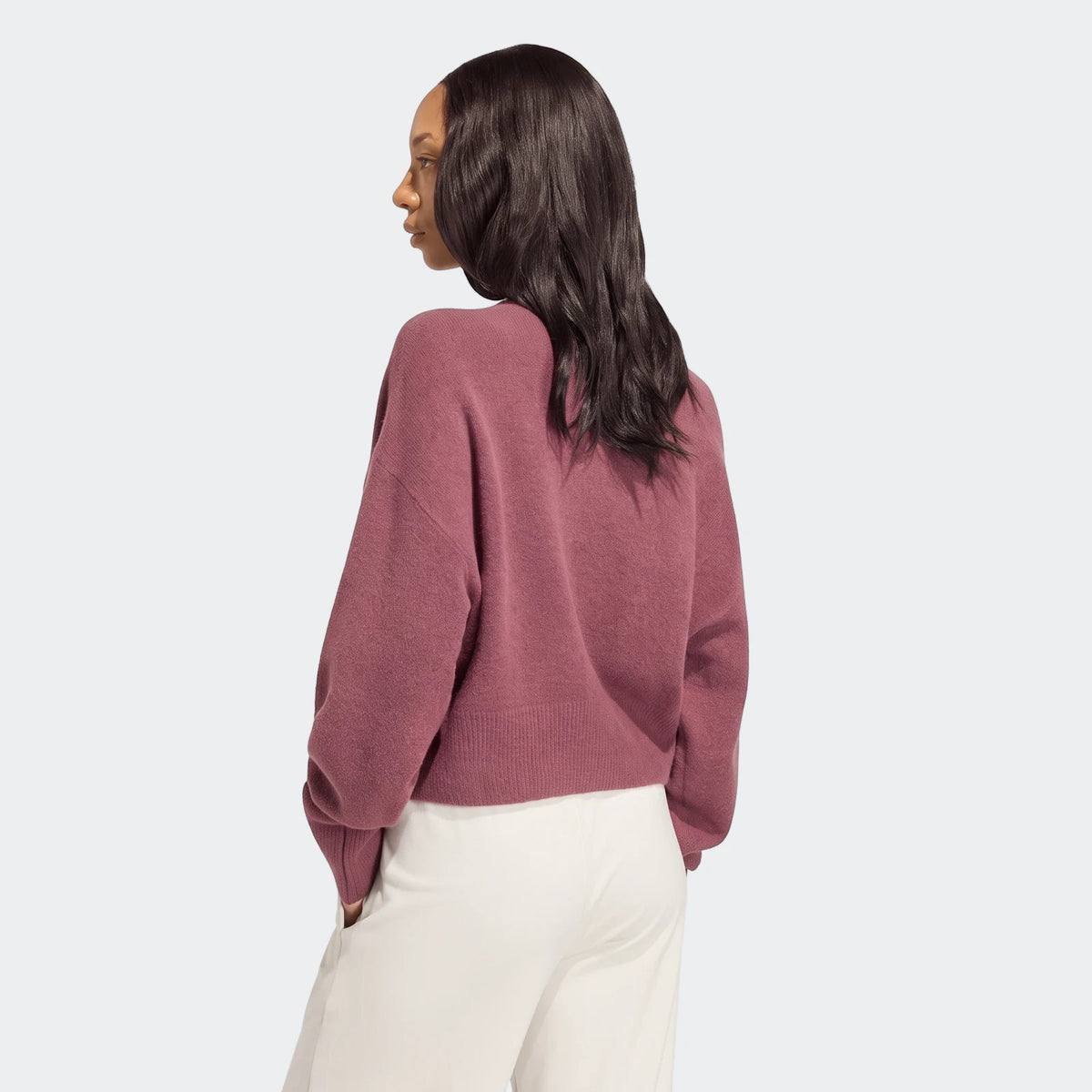 Woman wearing a mauve Essentials Knit Cardigan and light pants, shown from a back-side view against a white background.